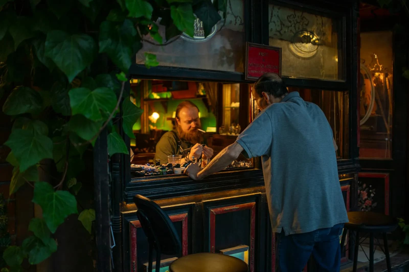 Dos hombres conversan a través de la ventana de una taquería rodeada de hiedra