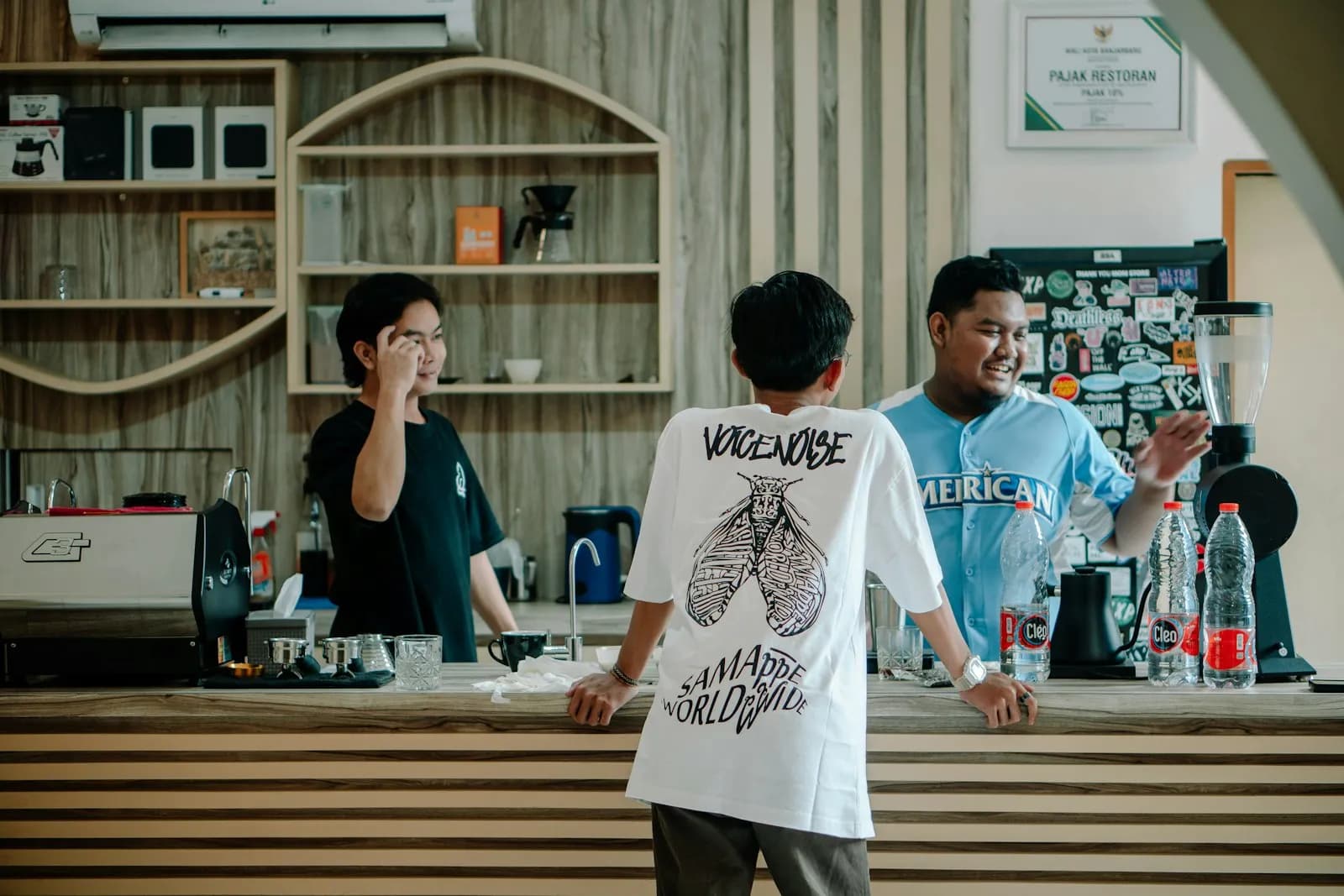 Tres personas conversan frente a la barra de un café con estantes de madera al fondo
