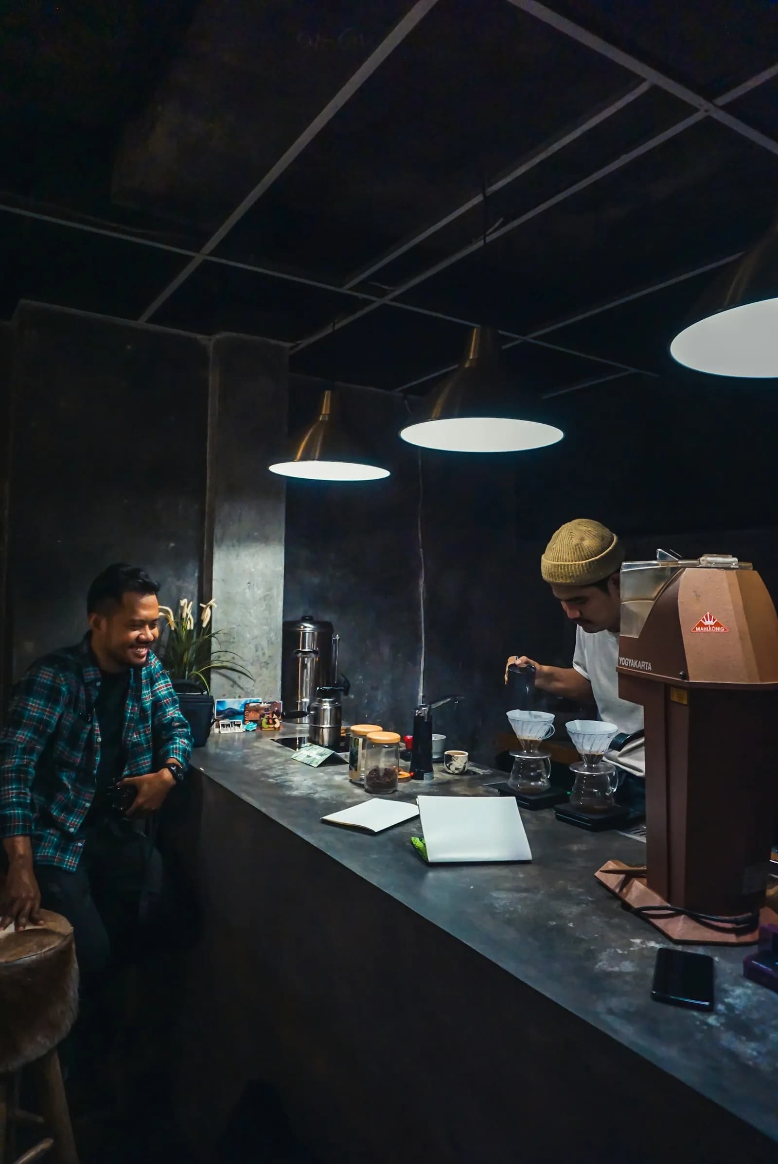Dos baristas en una cafetería oscura preparan café con filtros